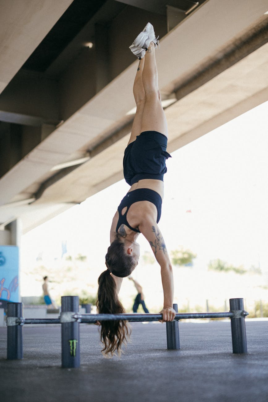 a woman in black shorts and sports bra doing hand stand while holding on metal bars